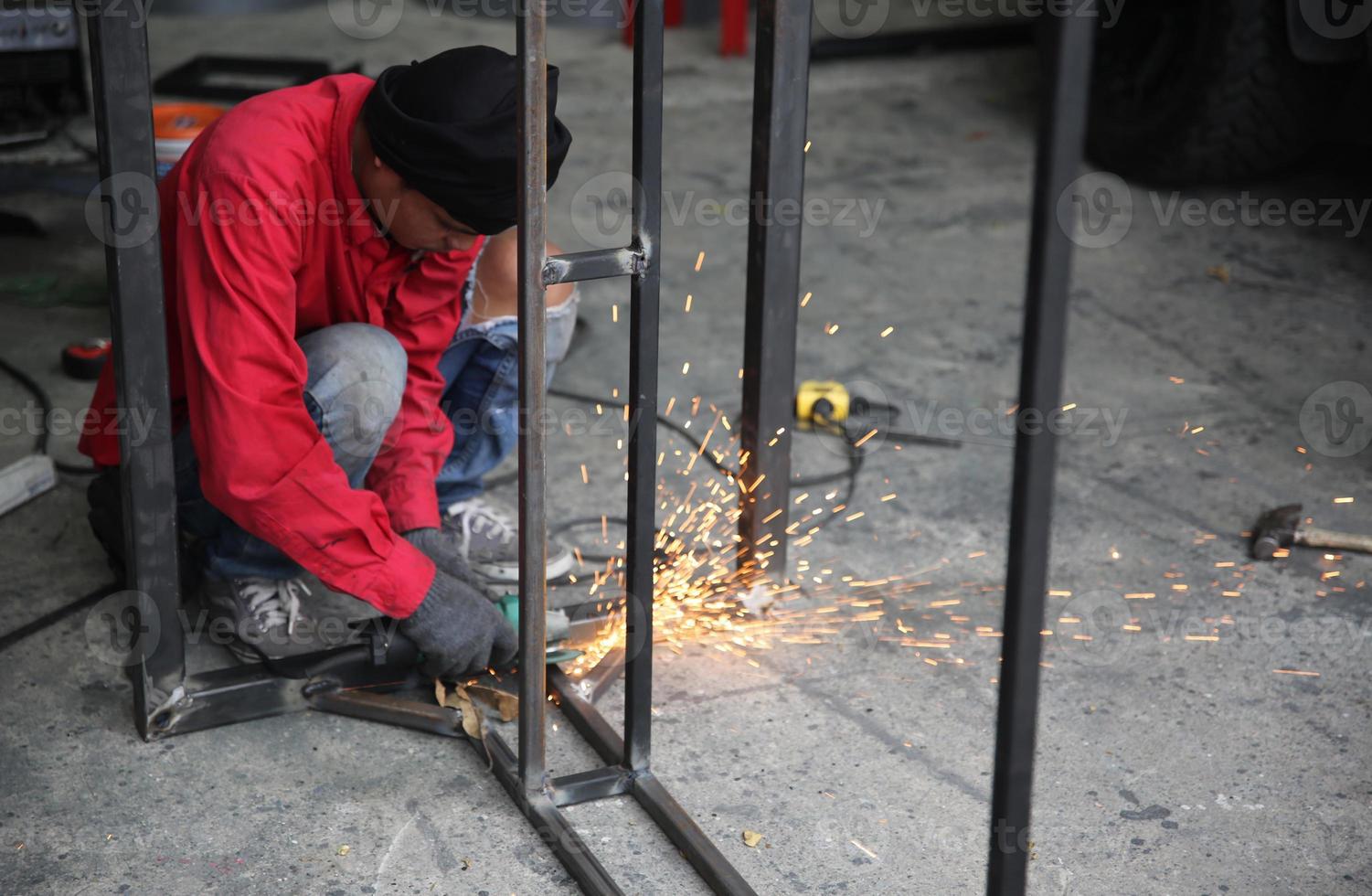 saldatore usato mola su acciaio in fabbrica con scintille, processo di saldatura presso l'officina industriale, mani con strumento nel telaio. foto