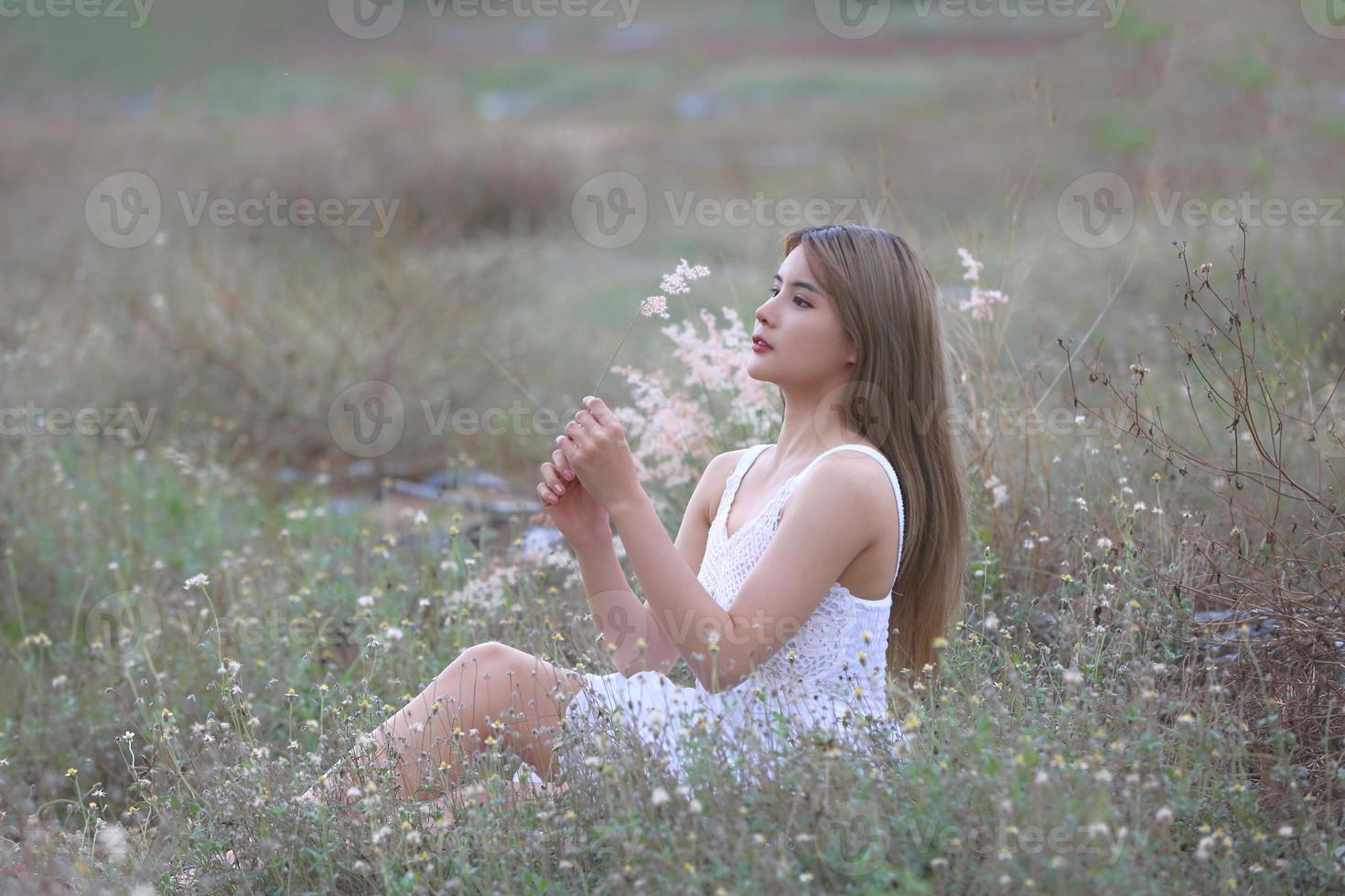 bella giovane donna seduta sul campo in erba verde e soffiando il dente di leone. all'aperto. Godi la natura. ragazza sorridente sana sul prato di primavera. concetto privo di allergie. libertà foto