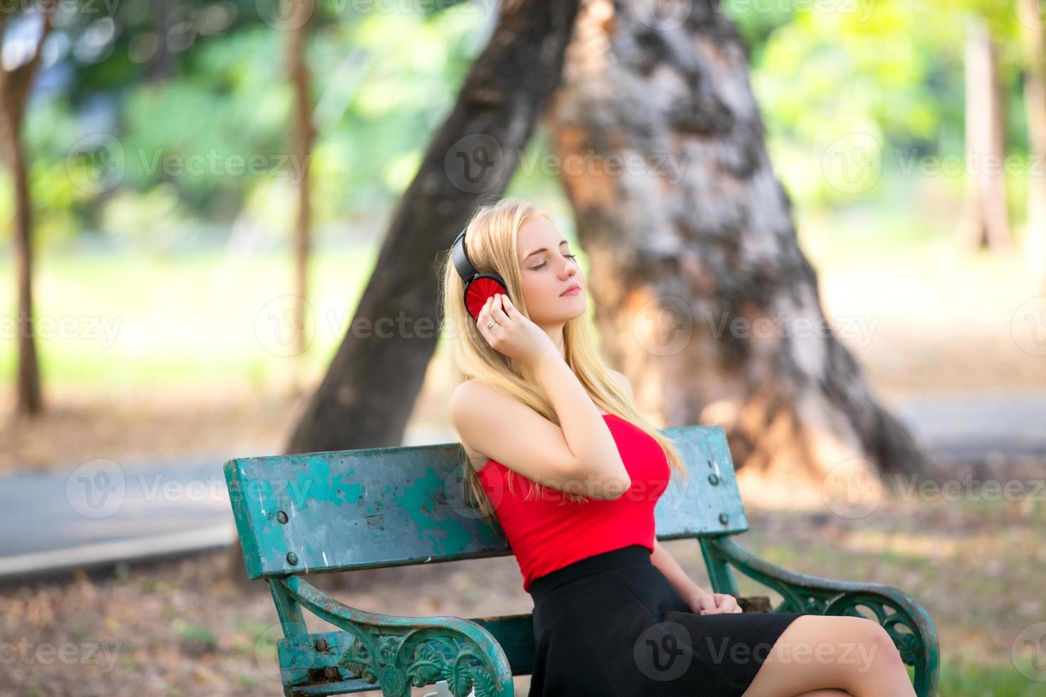 bella donna bionda in piedi mentre si ascolta musica in cuffia al parco. foto