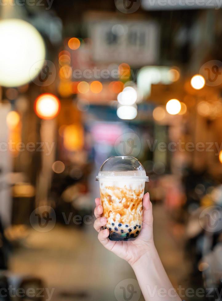 La giovane ragazza sta tenendo e mostrando una tazza di tè al latte con bolle di tapioca aromatizzato allo zucchero di canna nel mercato notturno di Taiwan sfondo, primo piano, bokeh foto