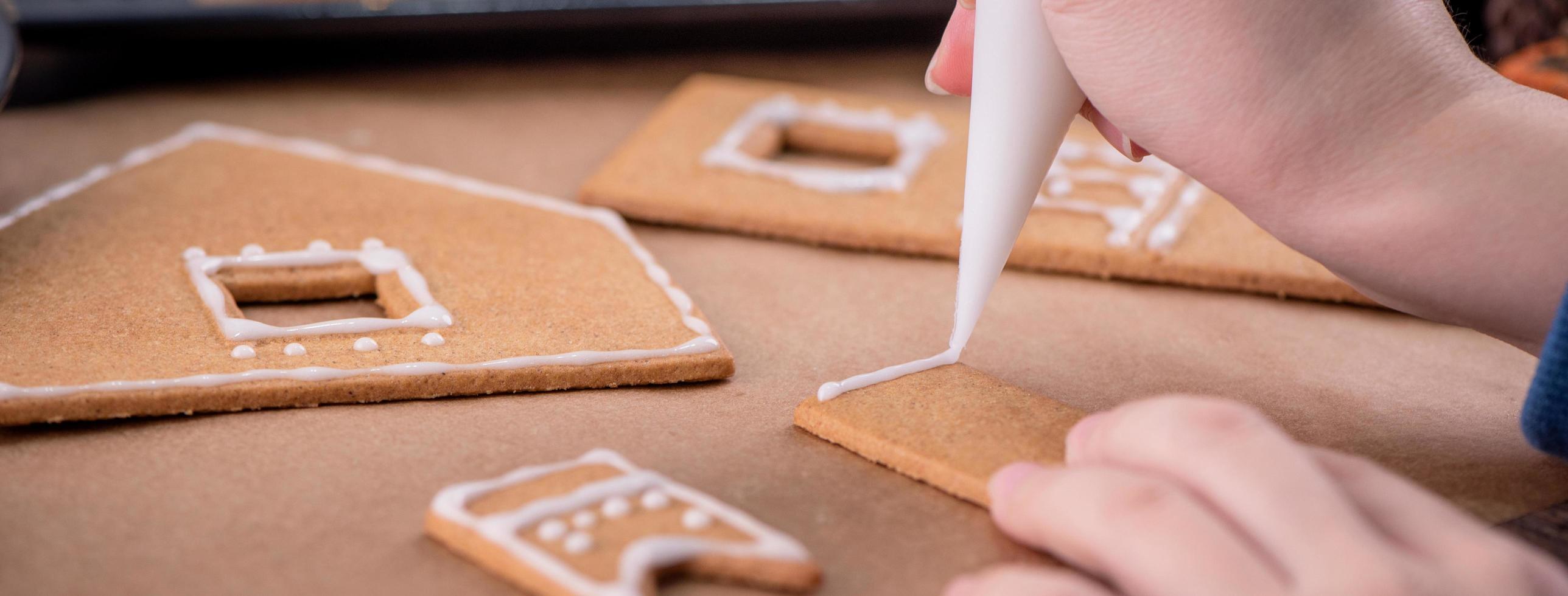 la donna sta decorando la casa dei biscotti di pan di zenzero con glassa bianca che guarnisce la crema di glassa sul fondo della tavola di legno, carta da forno in cucina, primo piano, macro. foto