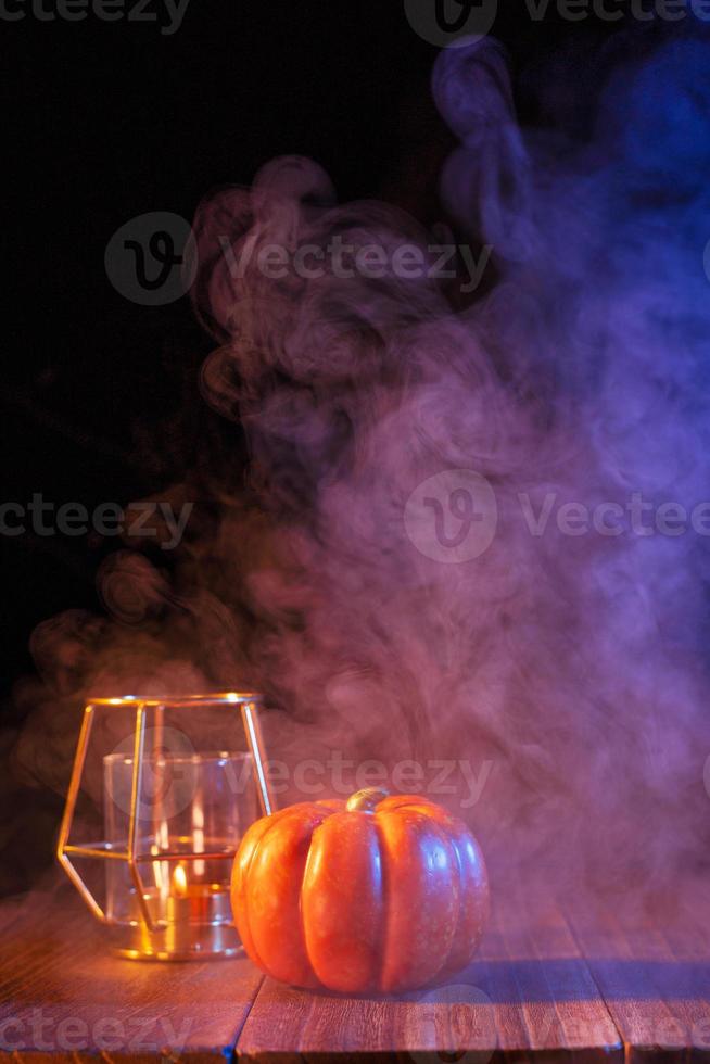 concetto di halloween, lanterna di zucca arancione e candele su un tavolo di legno scuro con fumo blu-arancio sullo sfondo, dolcetto o scherzetto, primo piano foto