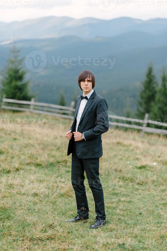 bello ed elegante sposo con la barba in abito a scacchi è in piedi sul ponte nella foresta. foto di sposi alla moda in scarpe di pelle marrone. ritratto rustico hipster.