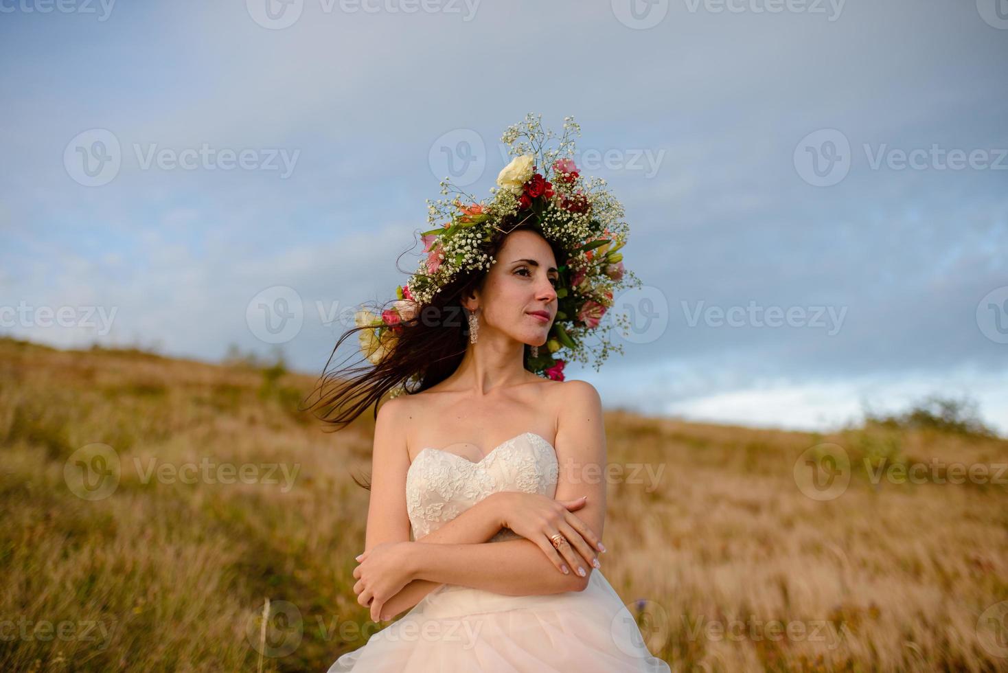 la sposa in un bellissimo vestito blu con una profonda scollatura sul retro con una corona di fiori bianchi sul capo si erge su uno sfondo di montagne e laghi foto