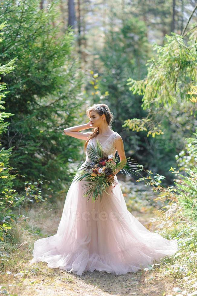 sposa felice in un abito da sposa rosa. la ragazza tiene in mano un bouquet da sposa. cerimonia di matrimonio in stile boho nella foresta. foto