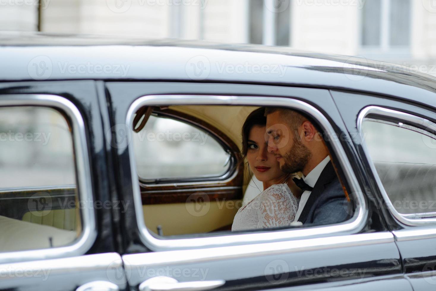 bella giovane sposa e sposo felici che guardano dall'auto retrò foto