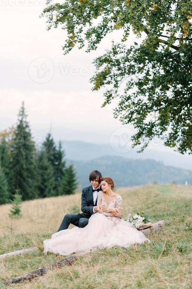 coppia attraente sposi novelli, momento felice e gioioso. l'uomo e la donna in abiti festivi si siedono sulle pietre vicino alla decorazione del matrimonio in stile boho. cerimonia all'aperto. foto