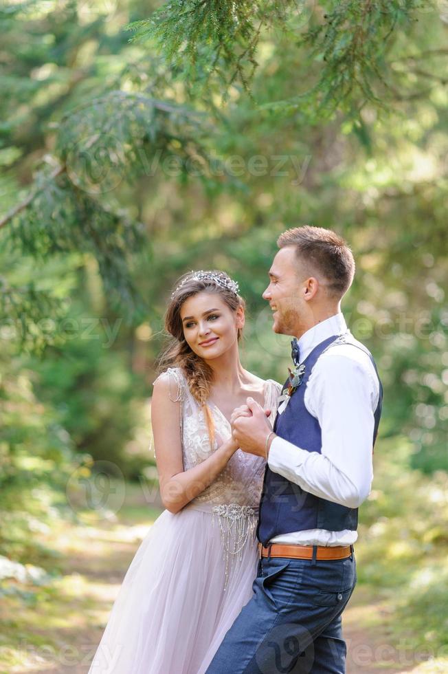 una coppia di sposini attraenti, un momento felice e gioioso. un uomo e una donna si radono e si baciano in abiti da festa. cerimonia nuziale in stile bohémien nella foresta all'aria aperta. foto