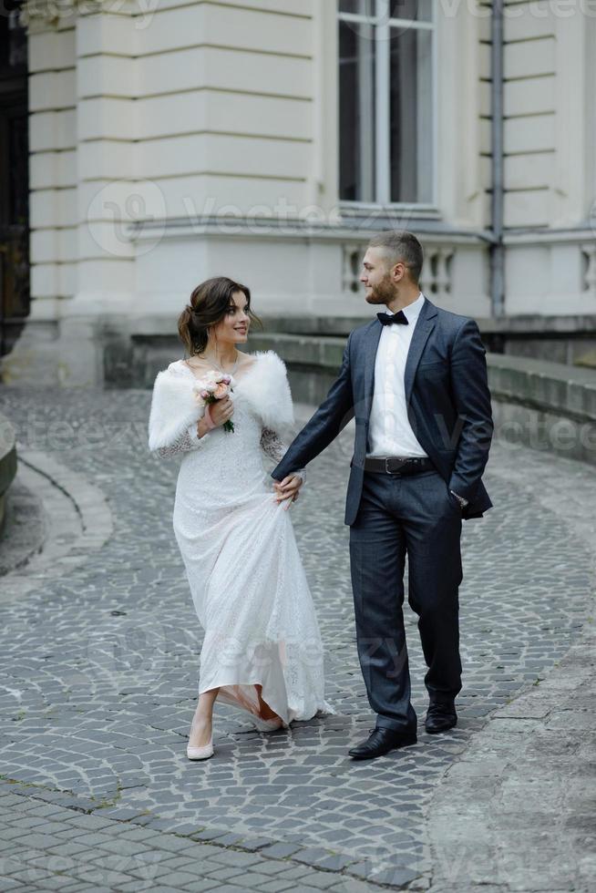 sposi in posa nella città antica. giovane sposa carina con un mazzo di fiori e l'abbraccio dello sposo. foto