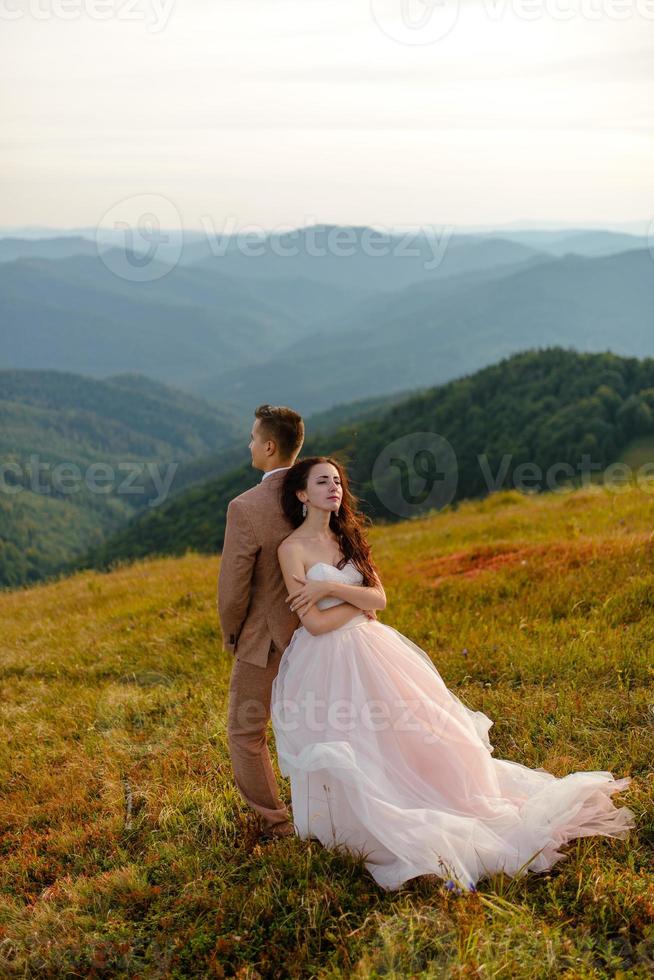 elegante giovane sposa e sposo stanno in barca su sfondo cloude cielo mare e montagne del montenegro foto