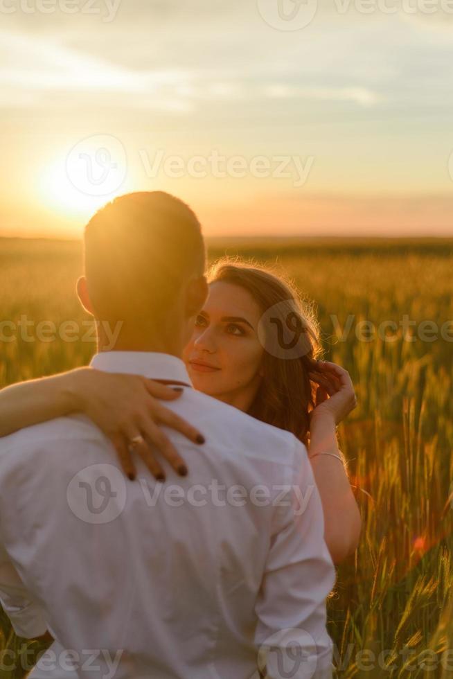 sposi in un campo di grano. la coppia si abbraccia durante il tramonto foto