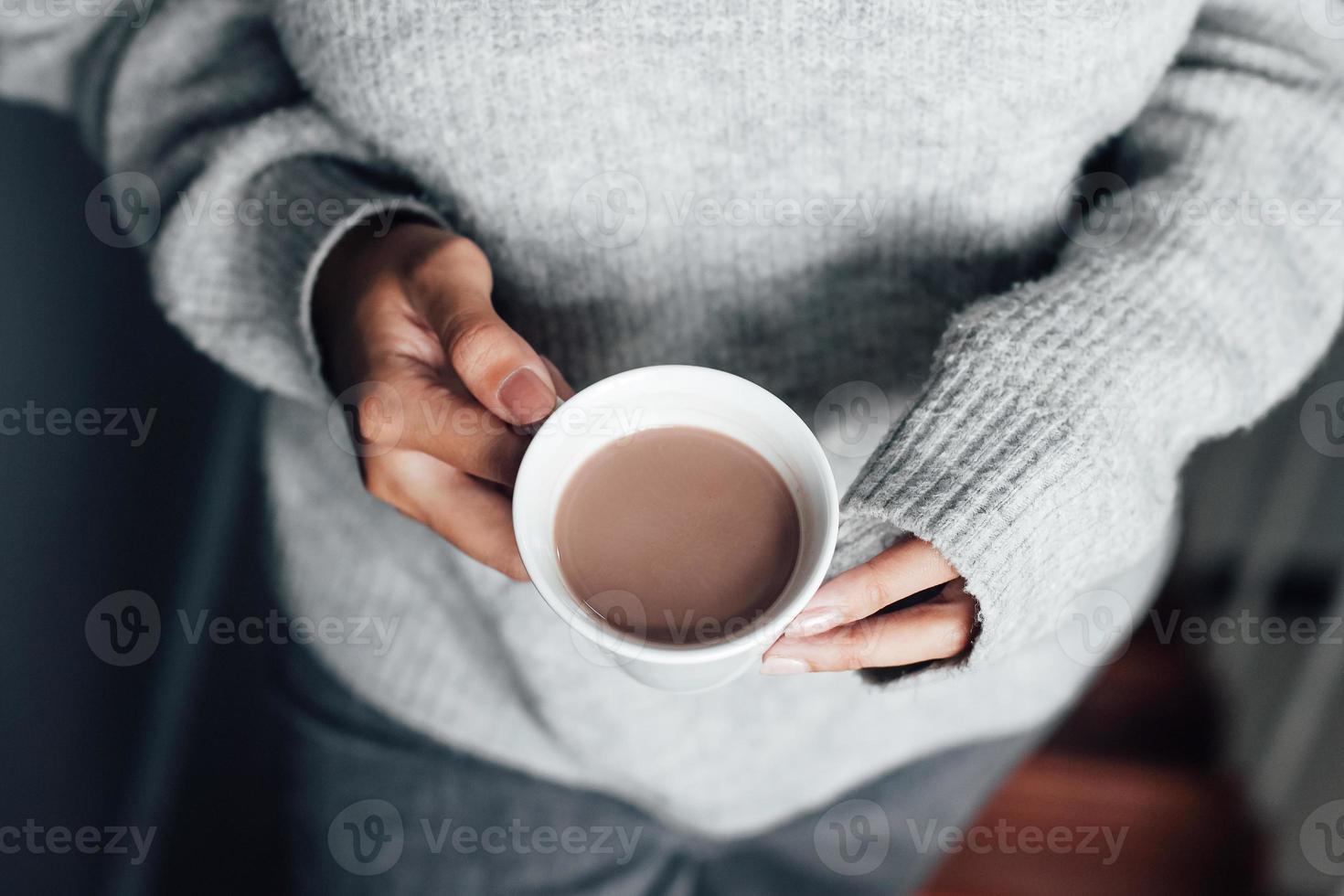 mani di donna che indossano abiti invernali a maniche lunghe con in mano una tazza di cioccolata calda foto