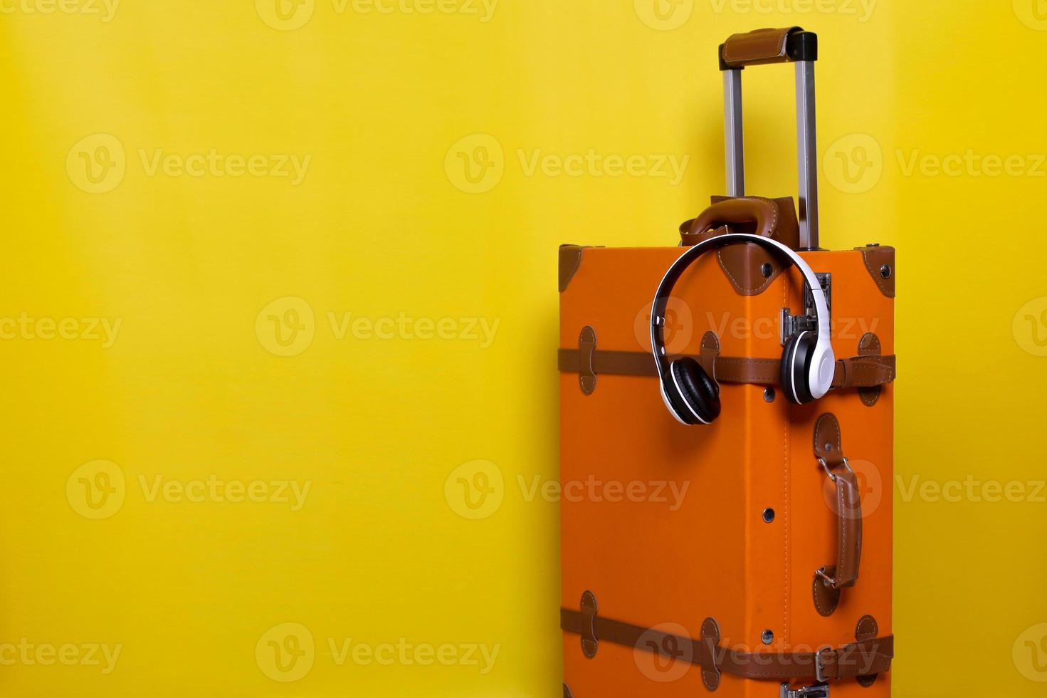 valigia vintage arancione con cuffie wireless isolate su sfondo giallo per il concetto di viaggio con uno stile minimale foto