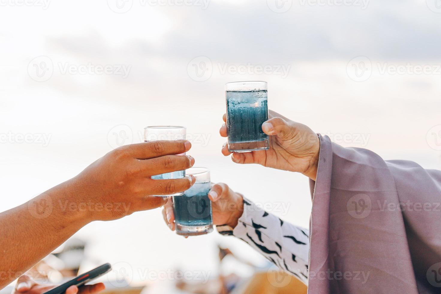 le mani delle persone tifano con un bicchiere di cocktail tropicale blu foto