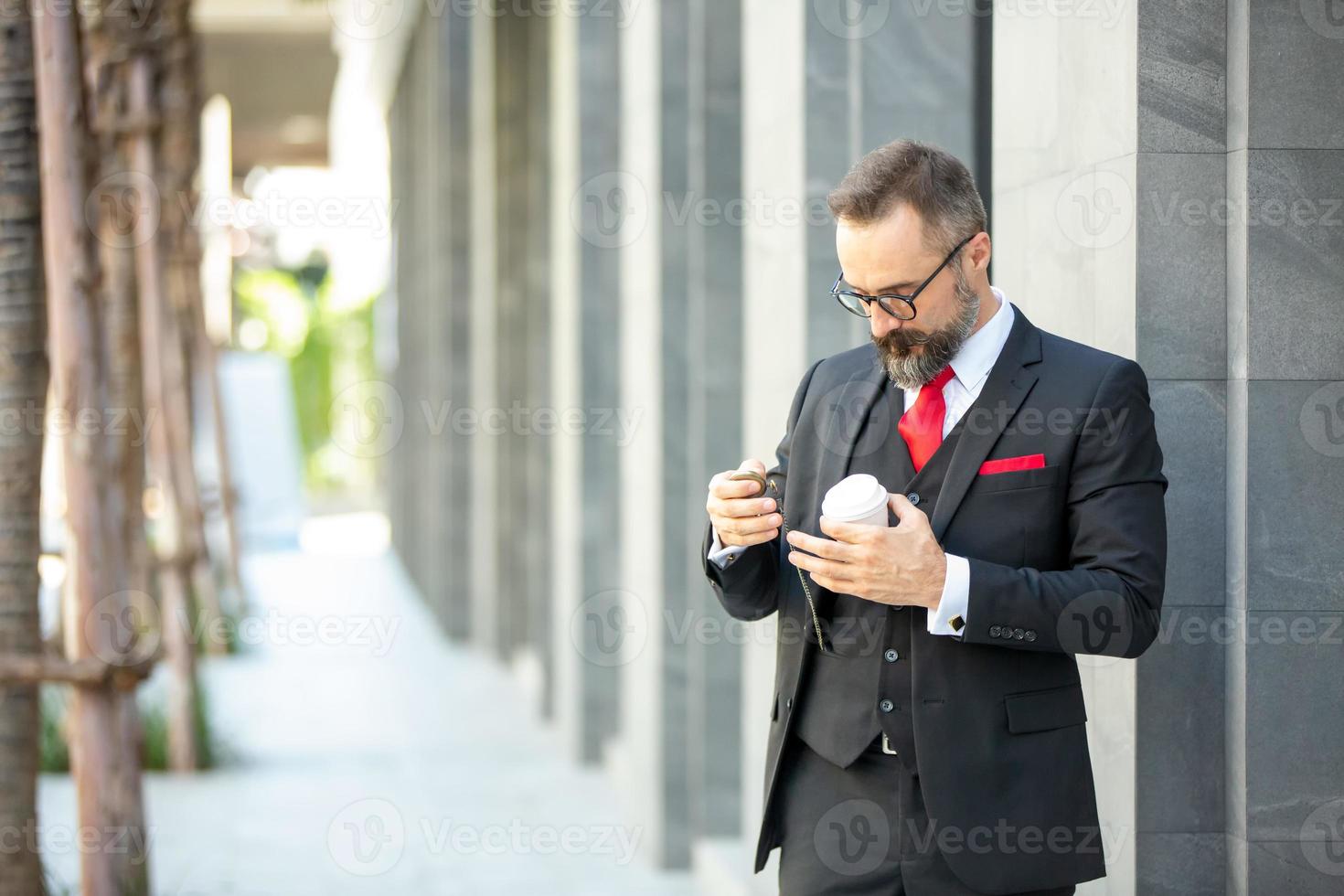 uomo d'affari hipster in giacca e cravatta in piedi con una tazza di caffè vicino all'ufficio all'aperto foto