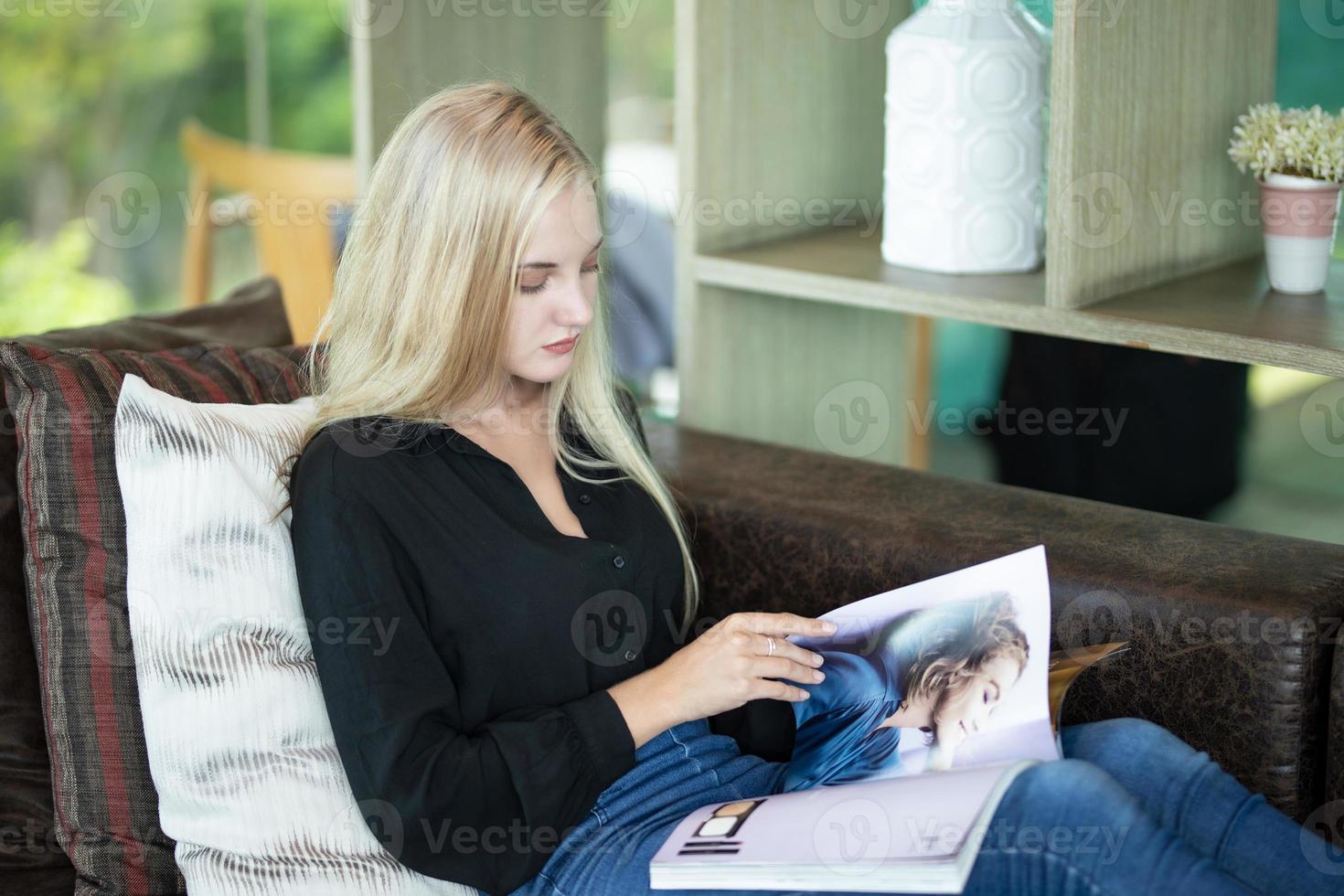 bella donna bionda che legge una rivista sul divano di casa foto