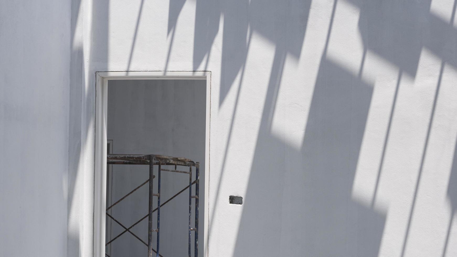 luce solare e ombra delle tegole sulla superficie del muro di cemento con impalcature nel telaio della porta all'interno del cantiere foto
