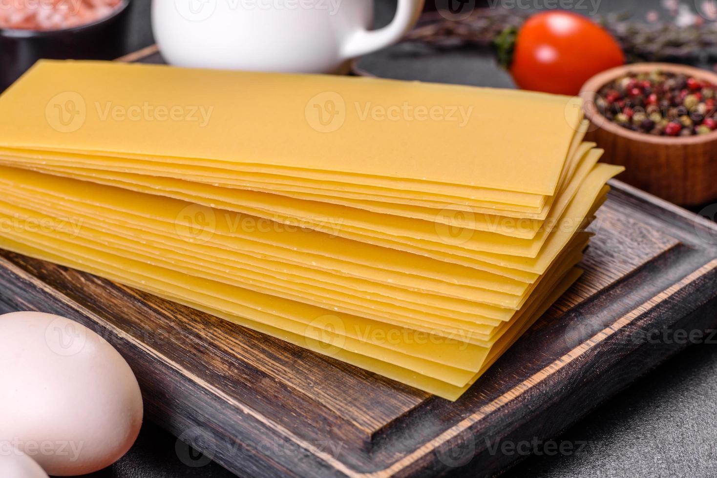 pila di fogli di lasagne su uno sfondo di cemento scuro. ingredienti per lasagne foto