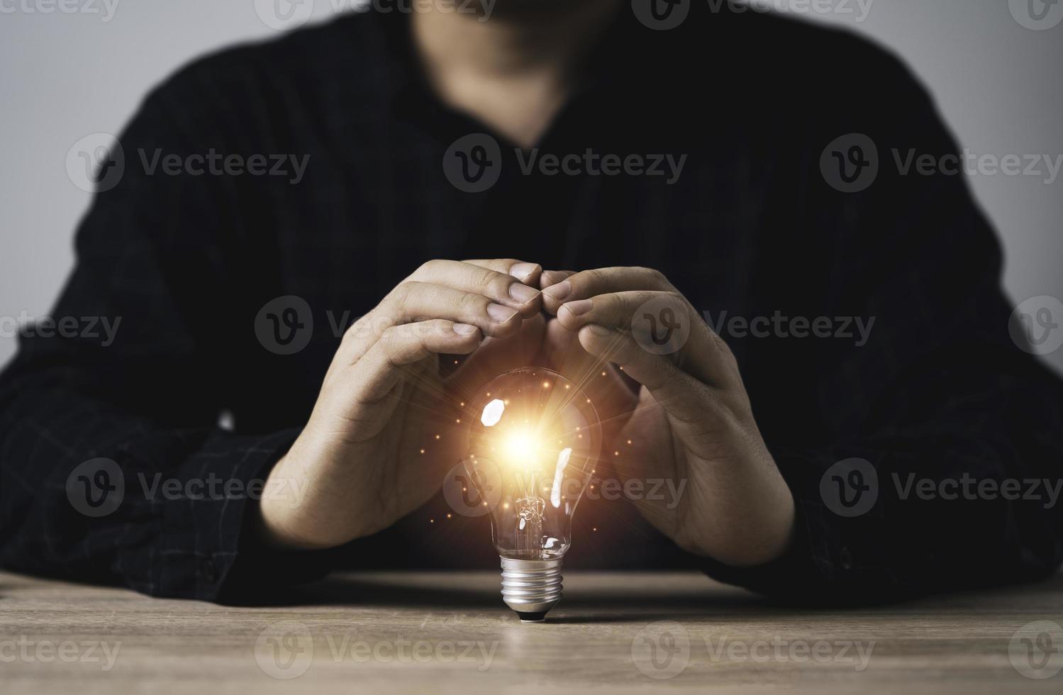 mano dell'uomo d'affari che protegge la lampadina incandescente con raggio di luce arancione sul tavolo di legno per l'ispirazione, idea di pensiero creativo e concetto di tecnologia di innovazione futura. foto