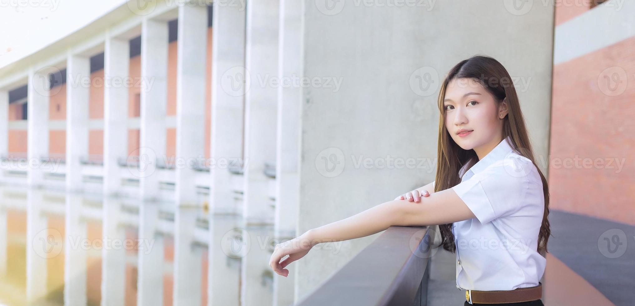 ritratto di uno studente tailandese adulto in uniforme da studente universitario. bella ragazza asiatica seduta sorridente felicemente all'università foto