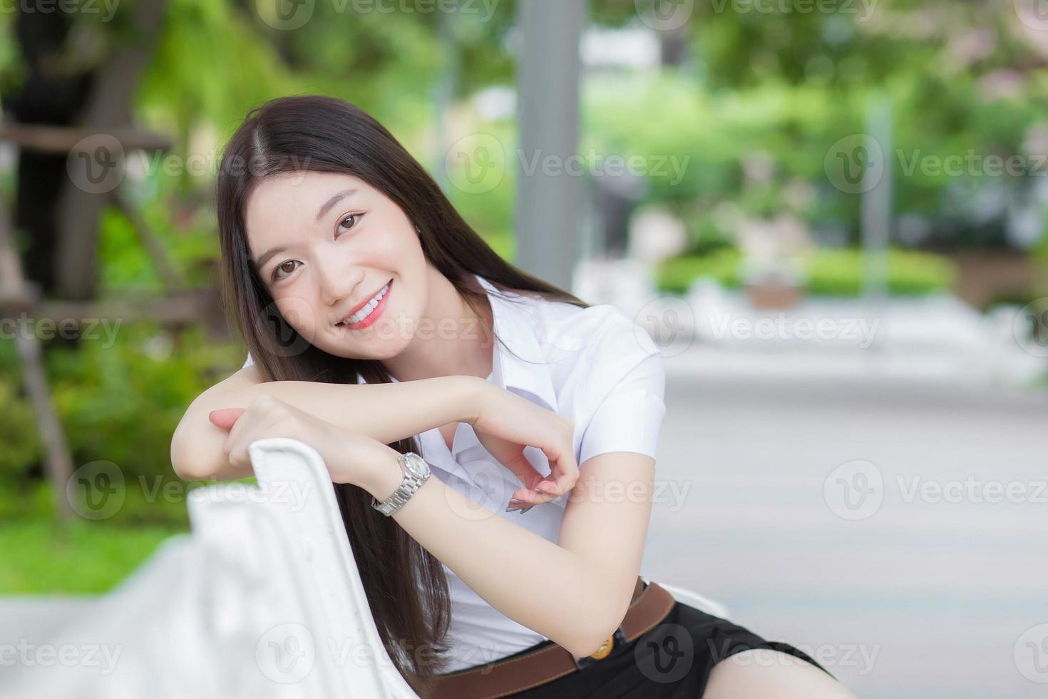 ritratto di uno studente tailandese adulto in uniforme da studente universitario. bella ragazza asiatica seduta sorridente felicemente all'università con uno sfondo di alberi da giardino. foto