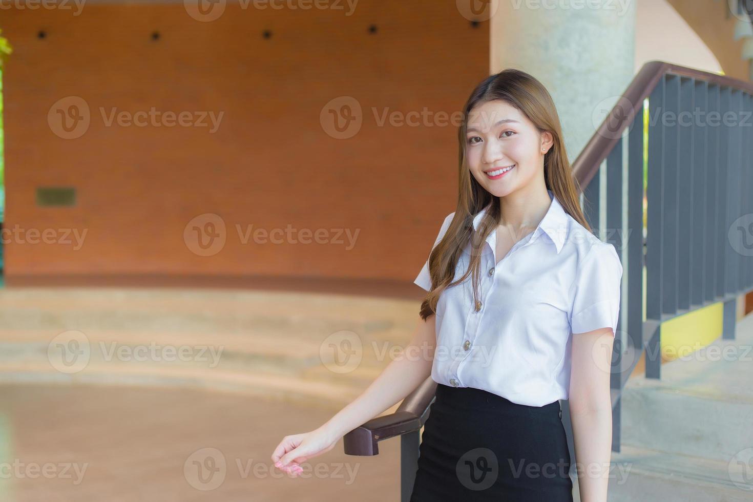 la bella studentessa asiatica della giovane donna sta sorridendo e sta esaminando la macchina fotografica nella priorità bassa dell'università foto