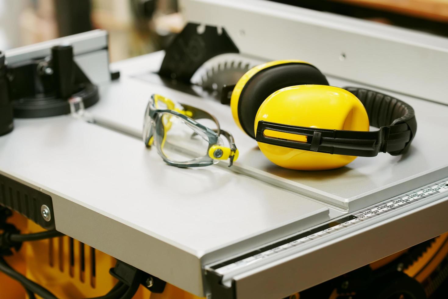 cuffie e occhiali di sicurezza sul tavolo della sega elettrica in officina. concetto di sicurezza sul lavoro. messa a fuoco selettiva foto