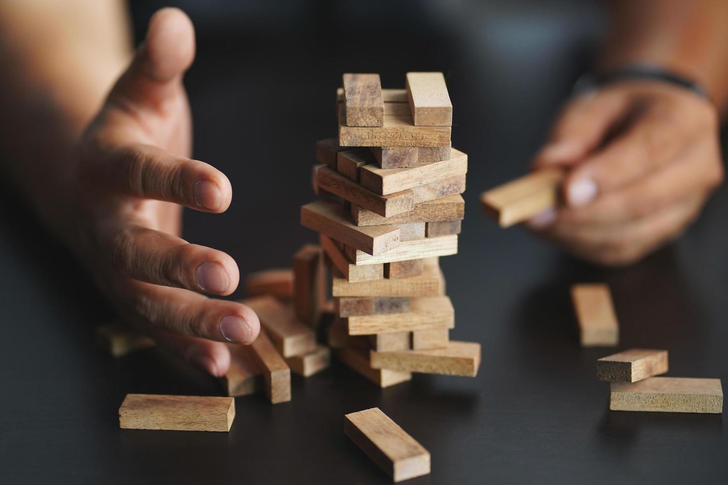 blocco di legno della copertura della mano dell'ingegnere e accumulo e impilamento di una torre di blocchi di legno sulla scrivania nera. pianificazione, rischio e strategia nel concetto di business. foto