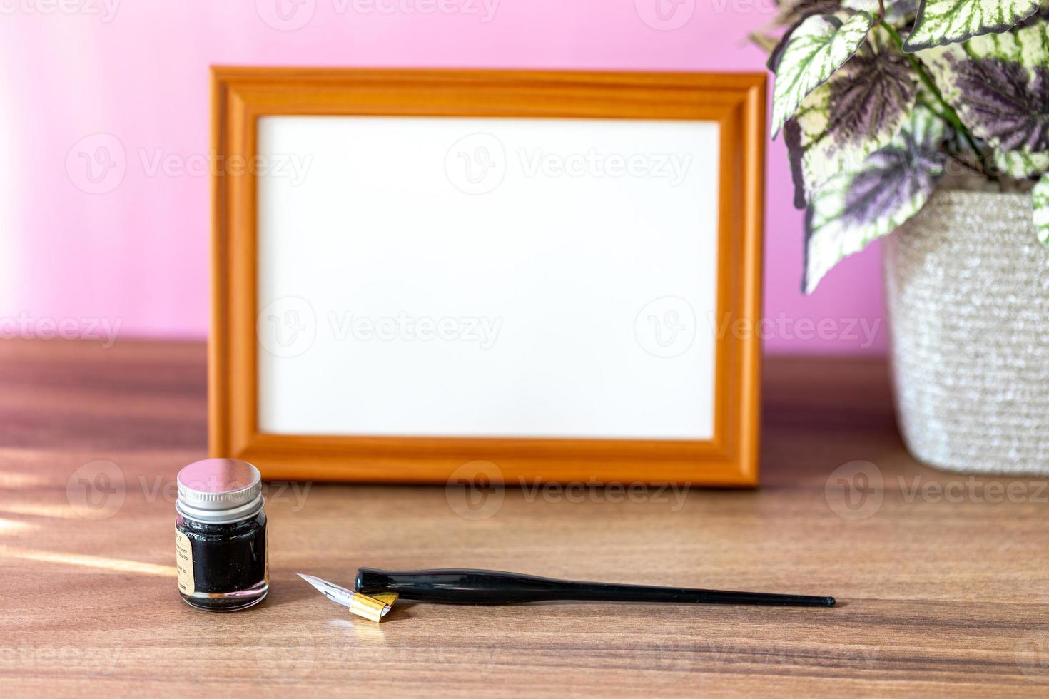 cornice in legno con paesaggio vuoto accanto a una piccola pianta d'appartamento e strumenti di calligrafia, pittura o visualizzazione di opere d'arte davanti al muro rosa foto