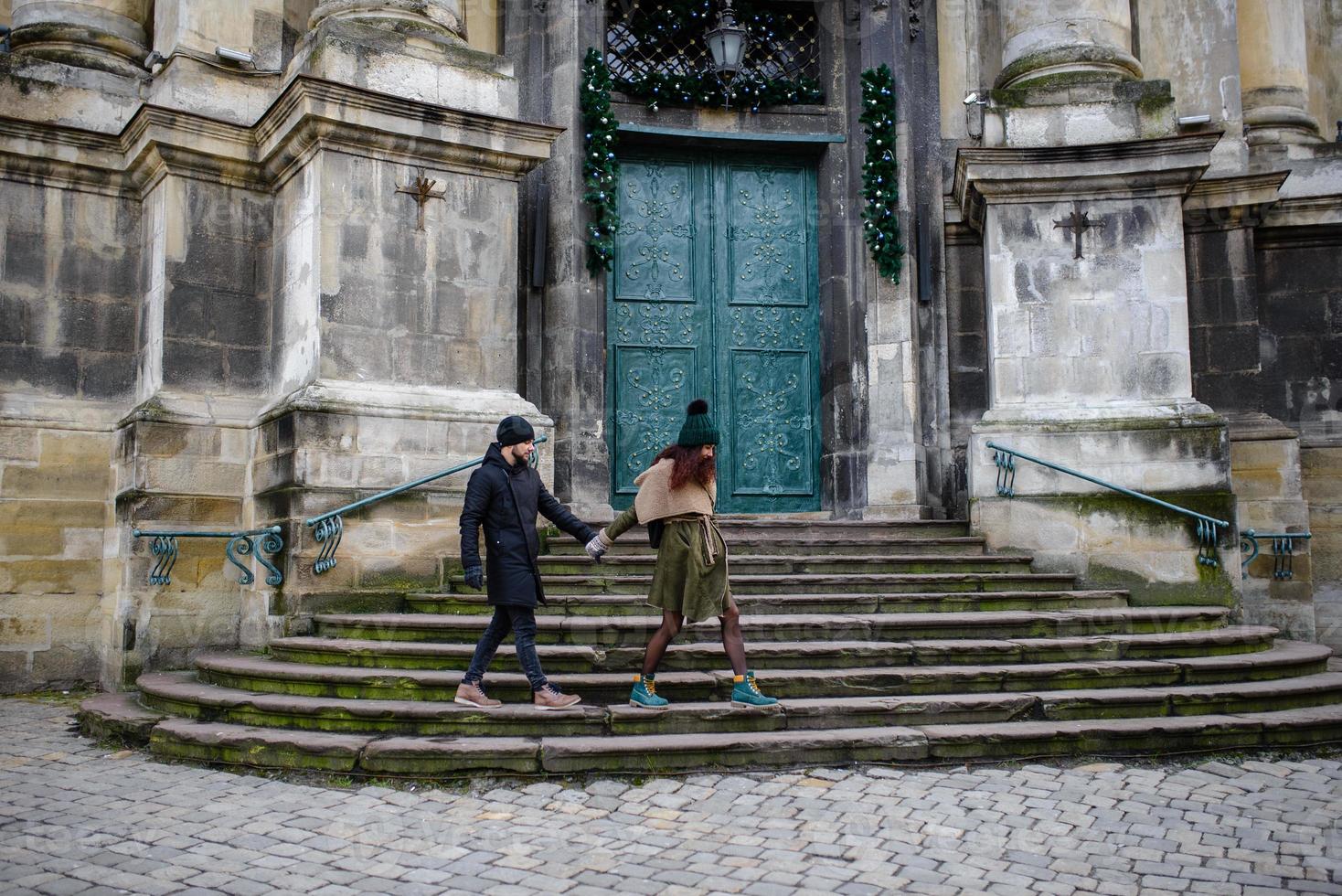 una giovane coppia alla moda passeggia per la città, la giovane donna ha le borse della spesa al braccio e l'uomo una tazza di caffè in mano foto