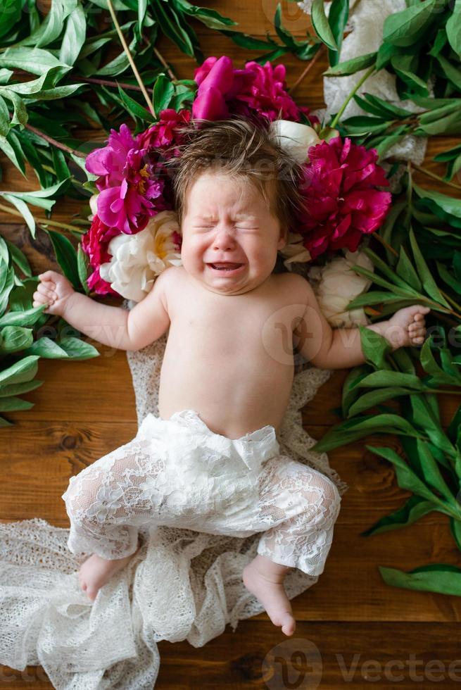 una bambina di due mesi giace su un tavolo con delle peonie. foto