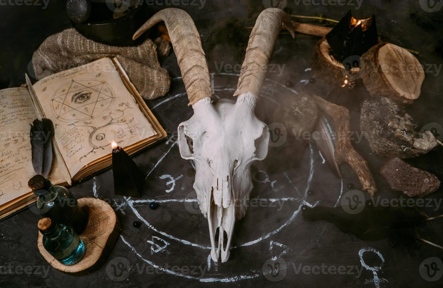 pala di capra bianca con le corna, vecchio libro aperto, incantesimi, rune, candele nere foto