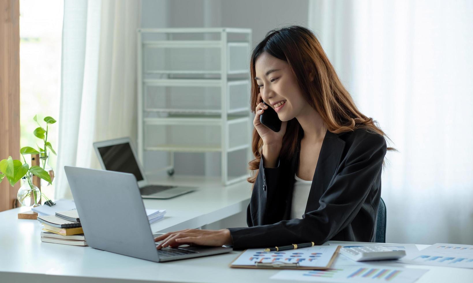 la donna asiatica d'affari ha la gioia di parlare al telefono, laptop e tablet sulla scrivania dell'ufficio. foto