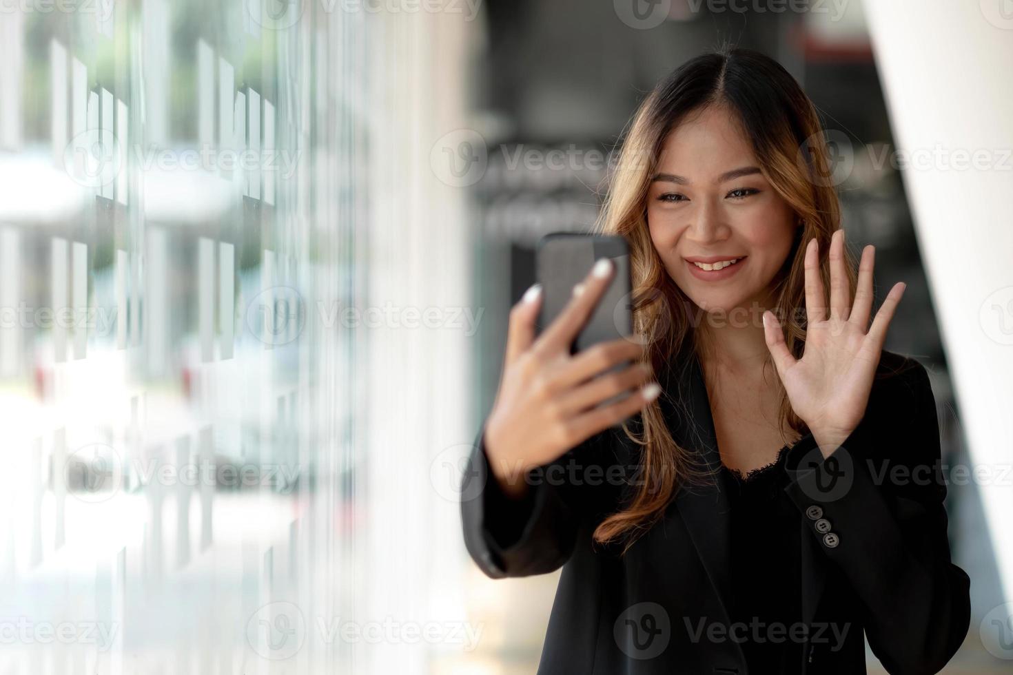 giovane donna di affari asiatica bella sorridente affascinante avendo una videochiamata con uno smart phone in ufficio foto