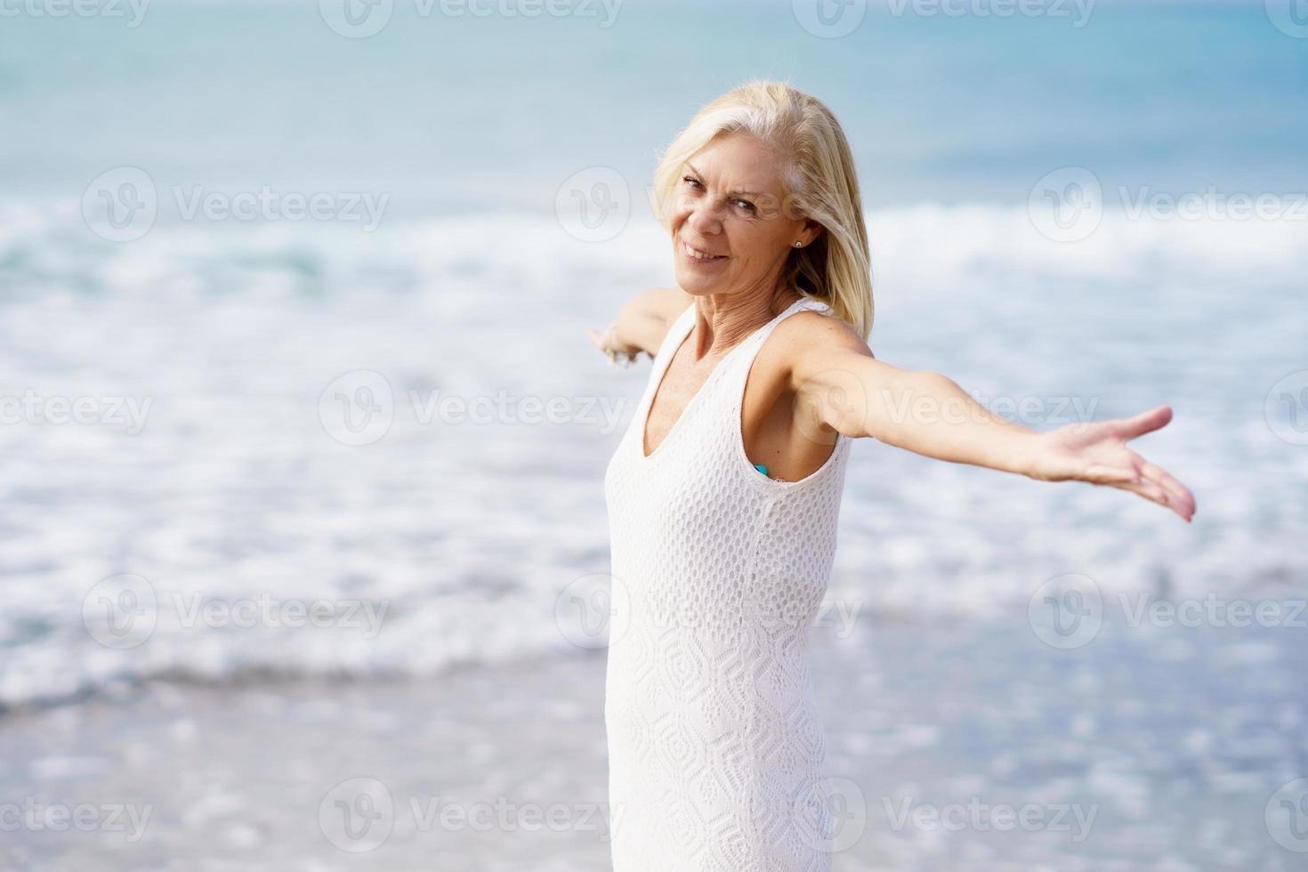 femmina matura aprendo le braccia sulla spiaggia, trascorrendo il suo tempo libero, godendosi il suo tempo libero foto
