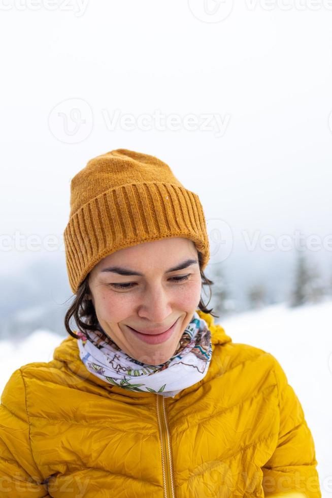 una donna con una giacca gialla tiene con lo smartphone in mano sullo sfondo delle montagne innevate foto