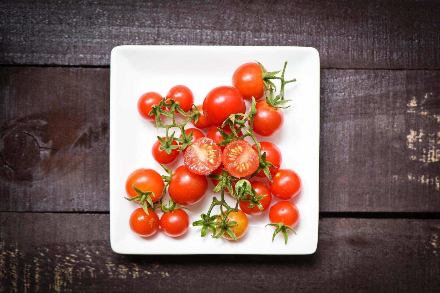 pomodori freschi su piatto bianco con vista dall'alto di sfondo scuro in legno foto