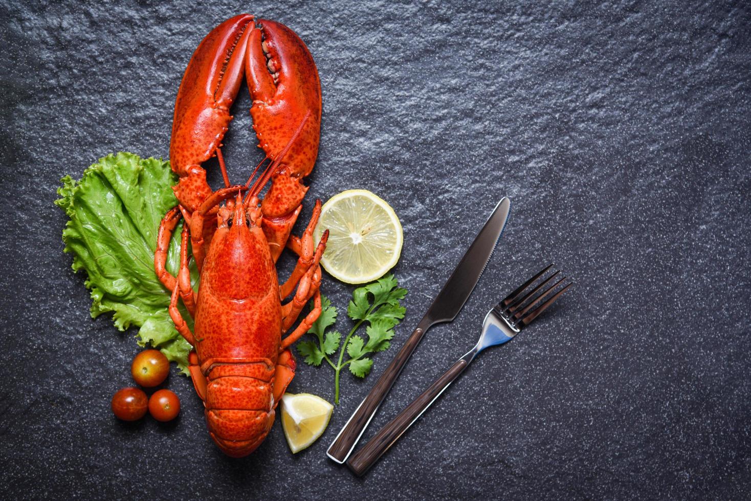 aragosta gamberetti frutti di mare con erbe aromatiche di limone e spezie su sfondo scuro e forchetta foto