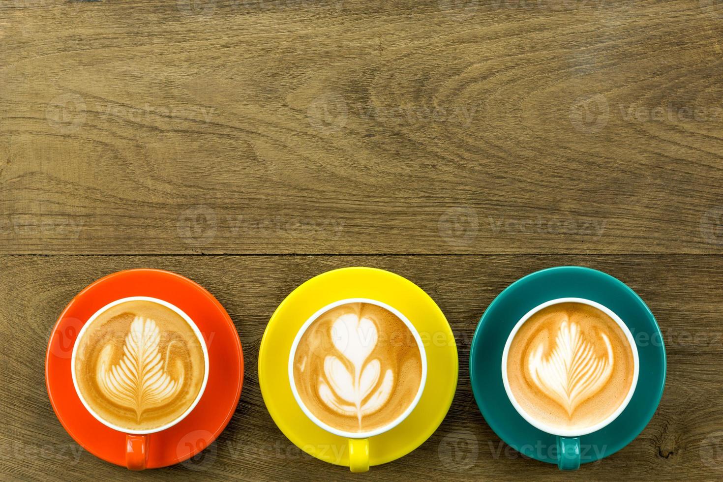 vista dall'alto di 3 caffè latte o cappuccino in tazza giallo arancio e blu scuro con latte art foto