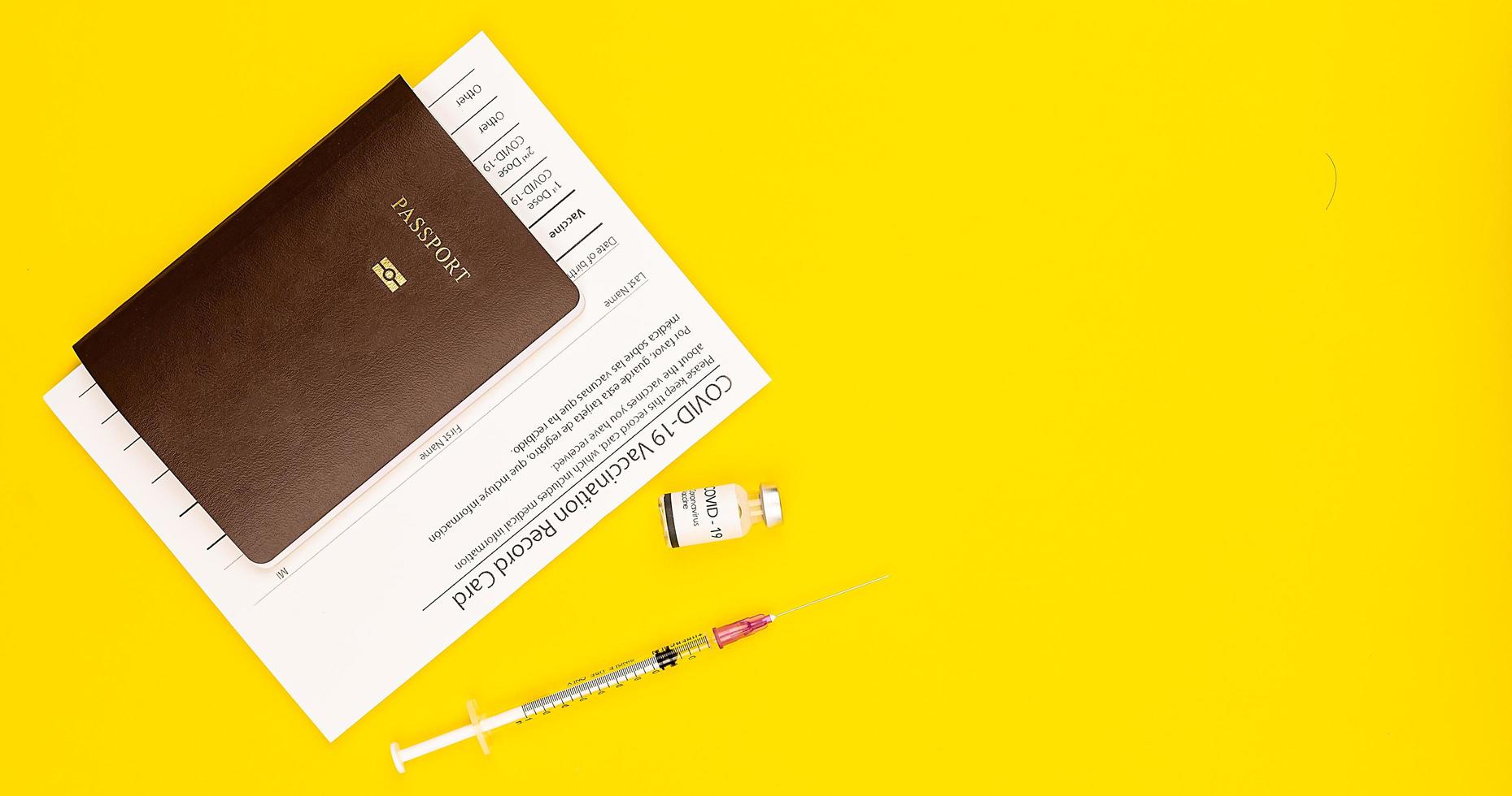 certificato di tessera vaccinale covid-19 e passaporto con flacone e siringa per il vaccino contro il coronavirus messi insieme su sfondo giallo con spazio per la copia. vista dall'alto e colpo piatto foto