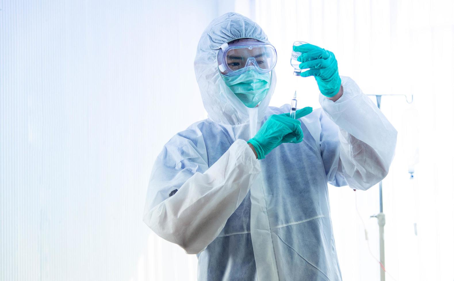 concetto di vaccinazione covid-19. il medico asiatico con guanto medico, maschera e tuta dpi tiene in mano la siringa e il vaccino contro il virus corona. foto