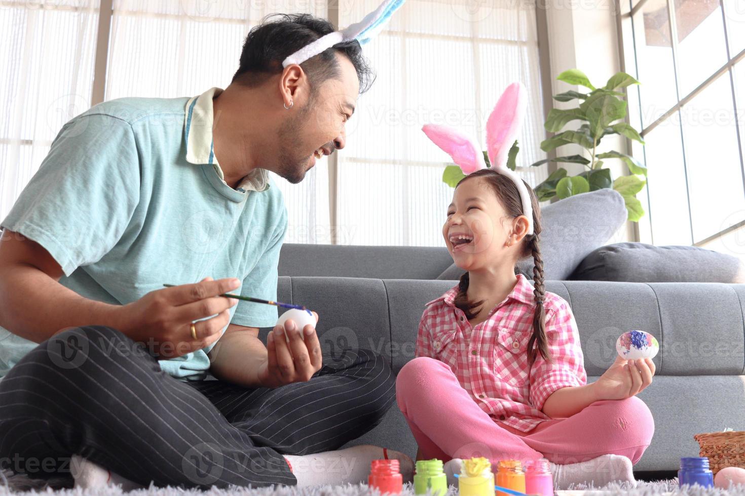 padre figlia prepara bellissime uova di Pasqua per la decorazione e la celebrazione dell'inizio della primavera, adorabile coniglietta rosa e suo padre con la fascia delle orecchie di coniglio che dipingono insieme uova colorate. foto