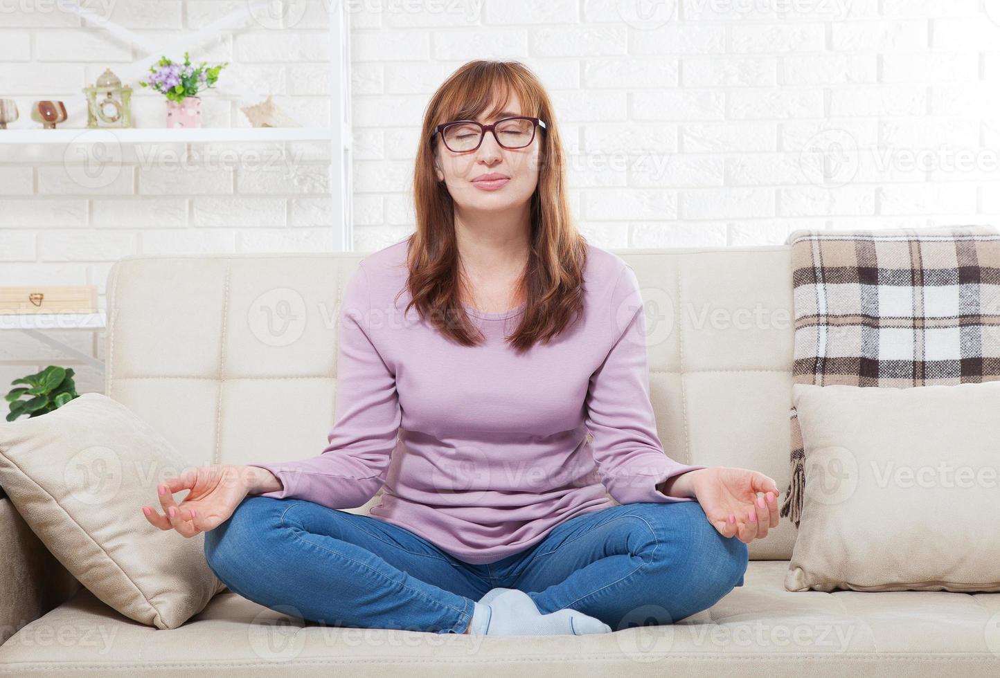 donna che fa yoga a casa in camera da letto. donna di mezza età che medita al chiuso. posa yoga. concetto di stile di vita e menopausa foto