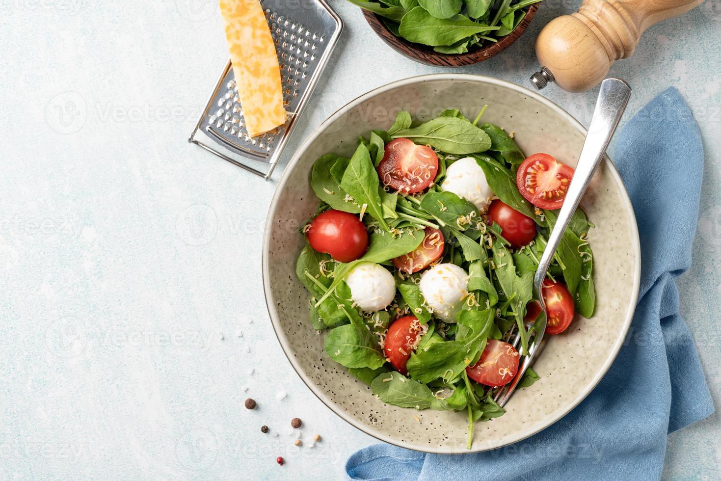 insalata fresca con rucola, pomodorini, mozzarella e formaggio a pasta dura su fondo di legno bianco. vista dall'alto foto