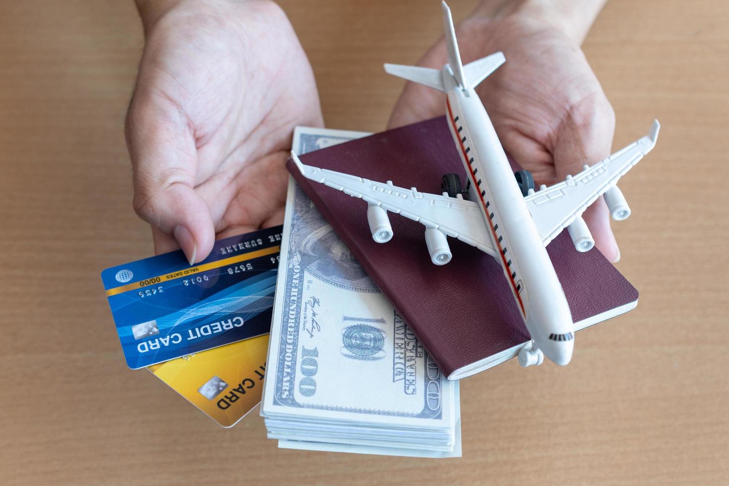 mani dell'uomo che tengono 100 banconote da un dollaro e aeroplano sul tavolo di legno. concetto di viaggio foto