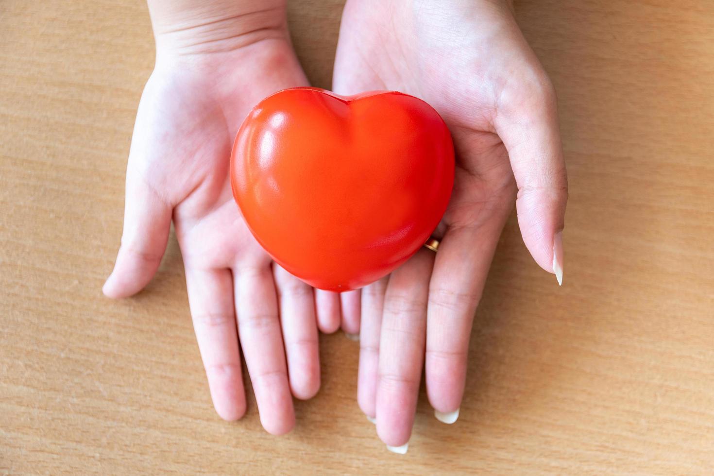 mani di madre e figlia che tengono cuore rosso, assistenza sanitaria, donazione e concetto di assicurazione familiare foto