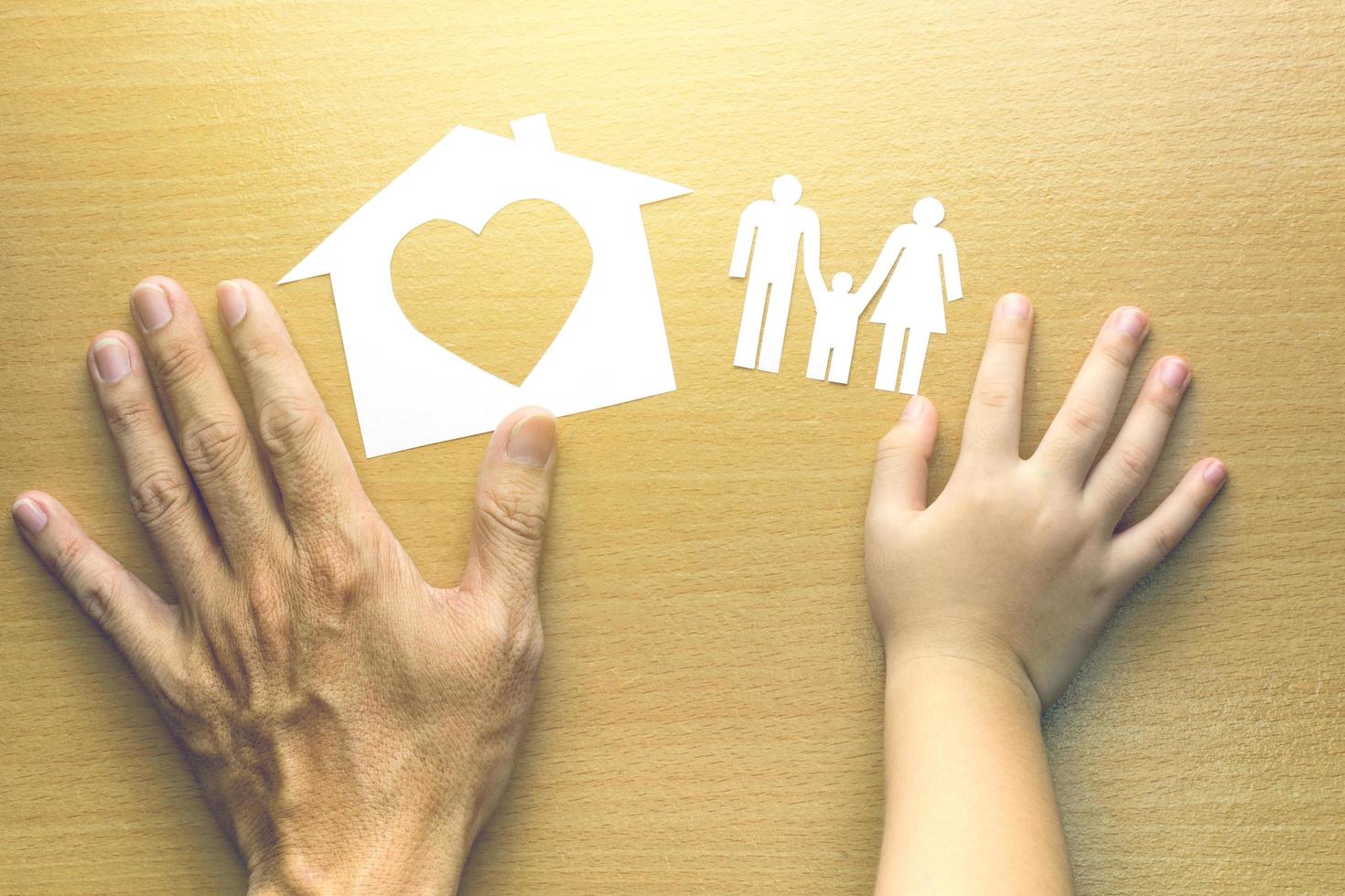 mani di padre e figlia con piccolo modello di casa e famiglia su fondo di legno foto