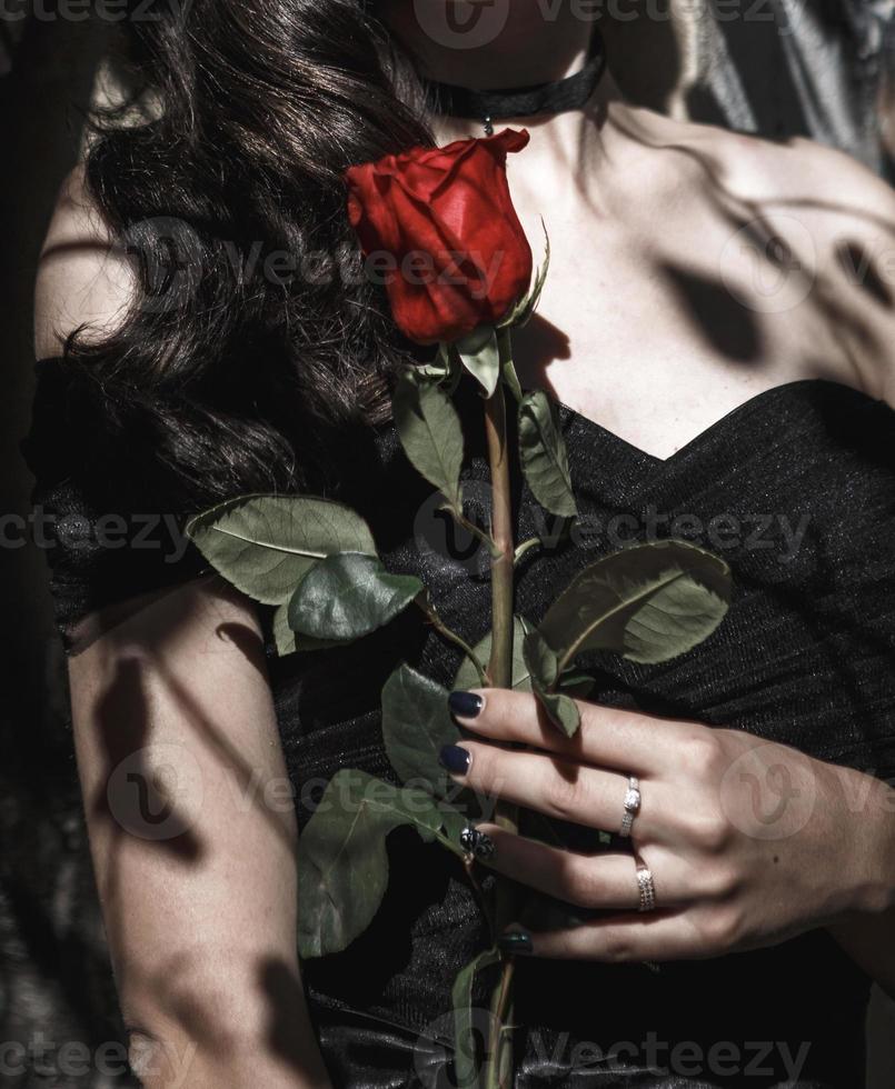 una ragazza con un vestito nero con una rosa rossa. stile gotico, mano femminile con unghie nere, simbolo di amore e morte, tristezza, perdita, rigorosa eleganza in nero foto