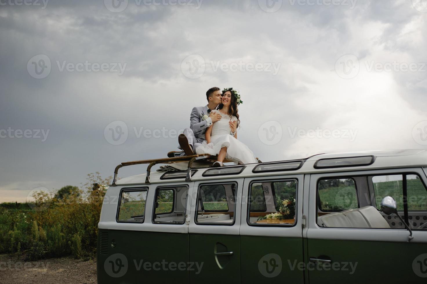 gli sposi hipster sono in piedi vicino al loro autobus retrò. foto