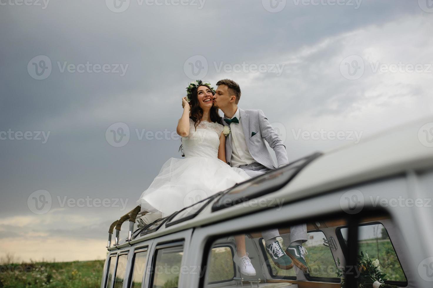 gli sposi hipster sono in piedi vicino al loro autobus retrò. foto